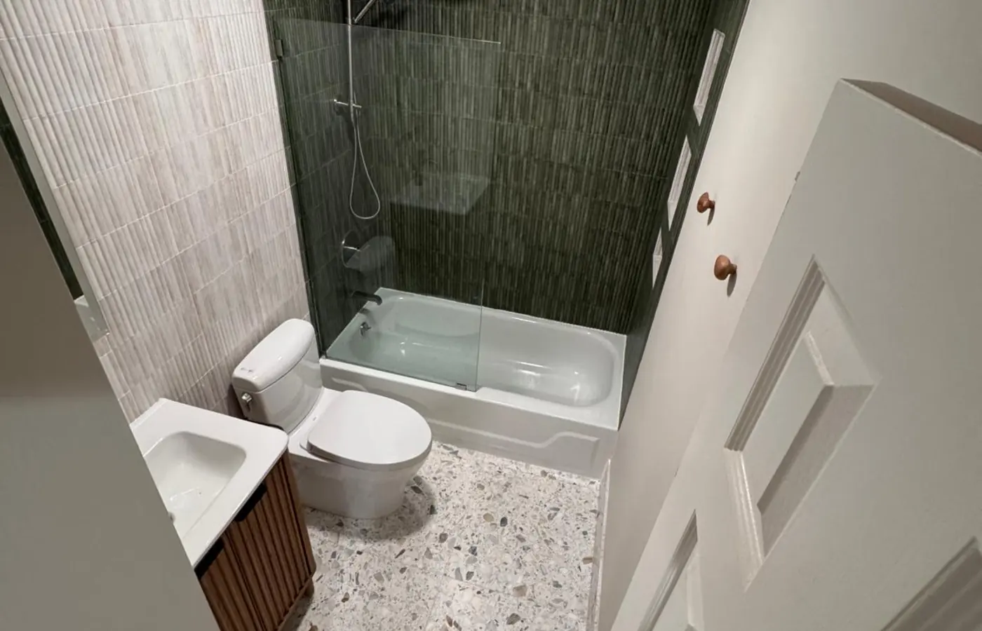 Finished bathroom with terrazzo look floor tile and a green tile shower